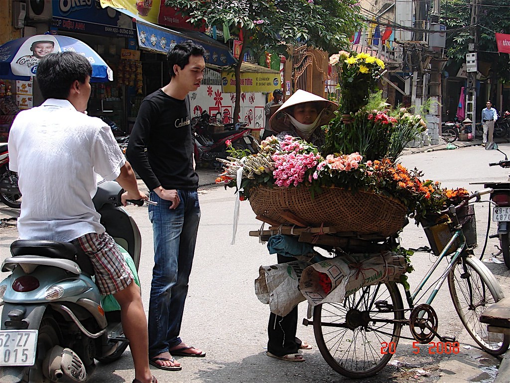 Hanoi street flower vendor standing behind a bicycle loaded with mixed bouquets in May 2008
