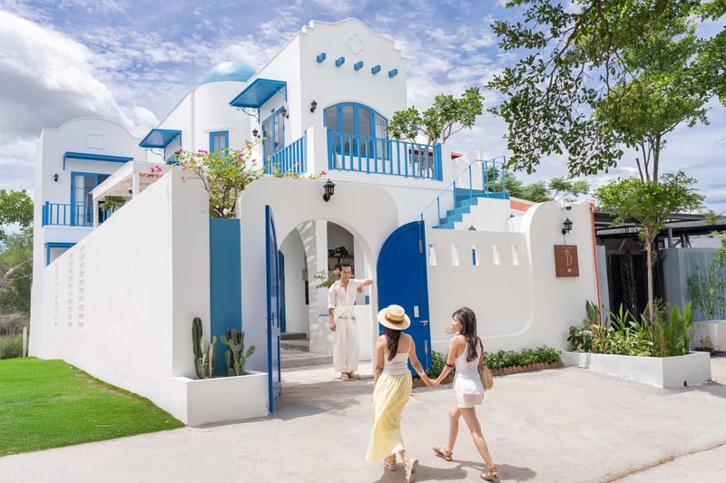 White Santorini-style pool villa with blue railings in Hoi An, guests walking to the entrance